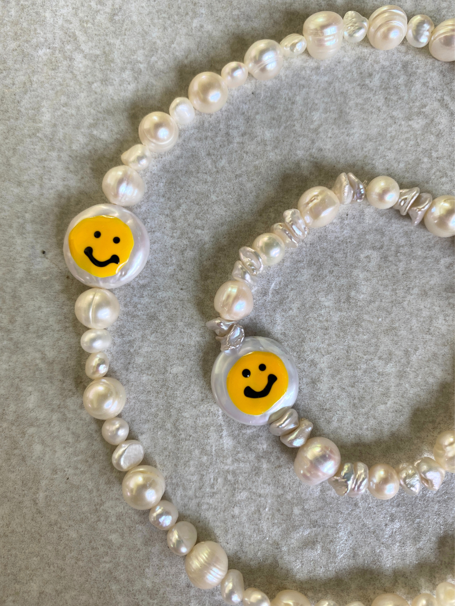 Smiley Kette und Happy Armband auf einem Steinhintergrund. Perlenkette und -armband mit Smiley-Perle